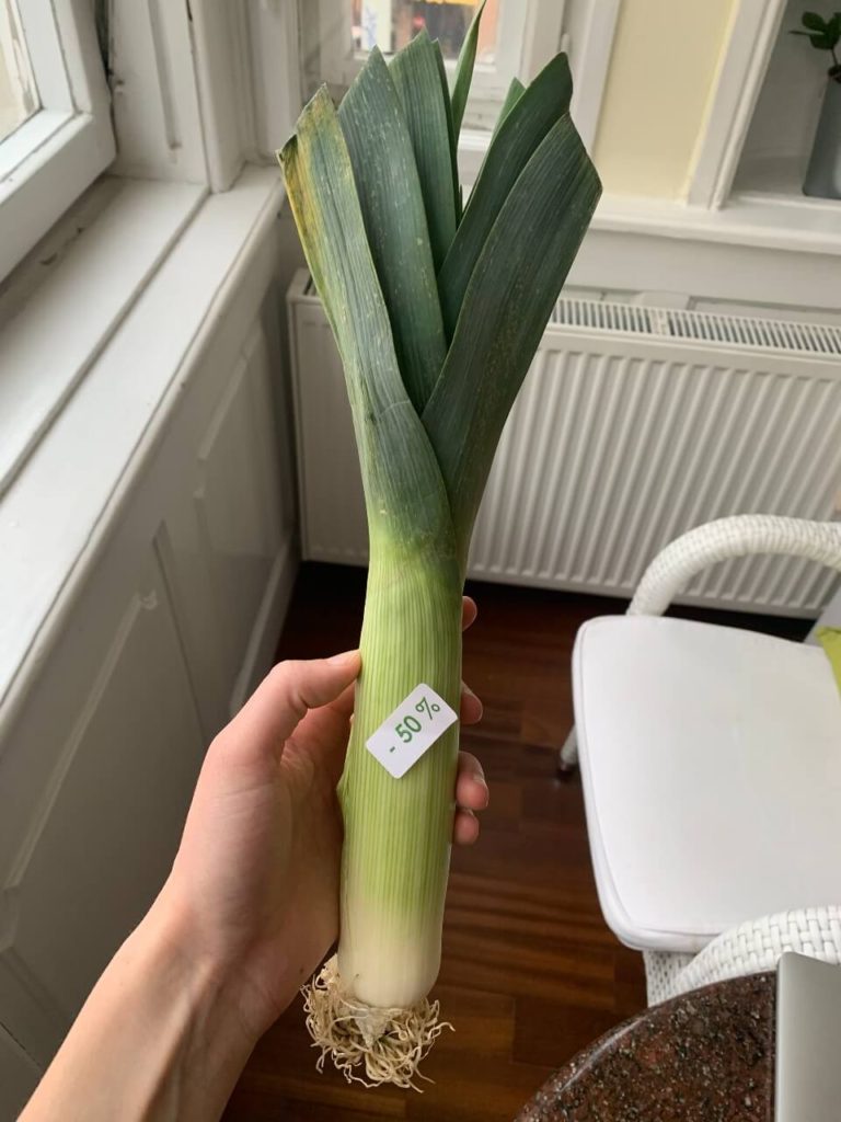 Leah holding a perfectly fine leek with a sticker on it that says it's discounted 50%.