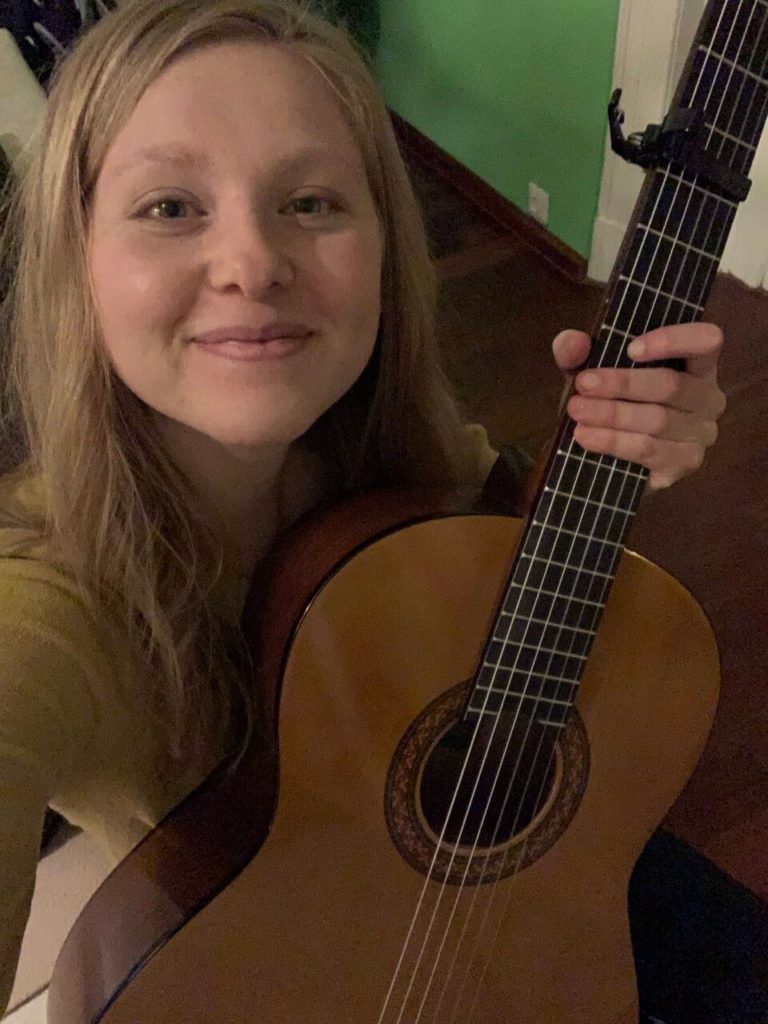 Leah, the author, holding a small tan guitar and looking at the camera.